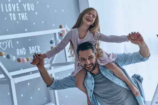 Vater trägt seine Tochter auf den Schultern und sie genießen Ihre Freizeit zuHause.